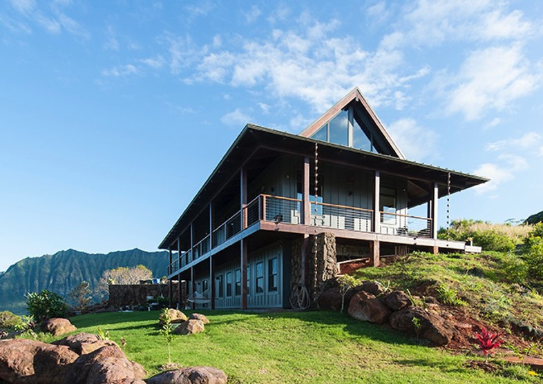 Hale Ahiki set into a green hillside beneath mountain peaks